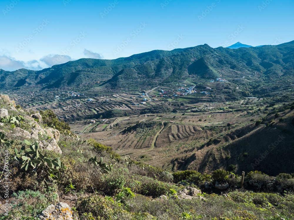 Dramatic lush green picturesque valley with old village Las Portelas. Landscape with sharp rock formation, hills and cliffs seen from mountain road, Tenerife, Canary Islands, Spain. sunny winter day