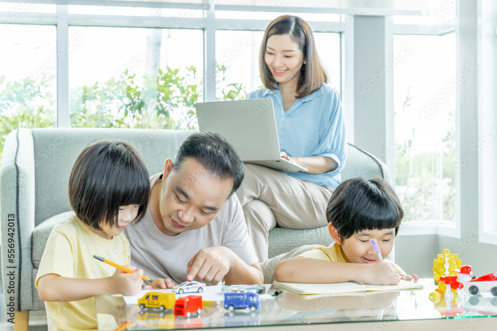 Happy Asian family male and female parents Teaching or helping with their children's homework. On holiday. Staying at home happily. Happy Asian family male and female parents Teaching or helping with their children's homework. On holiday. Staying at home happily.