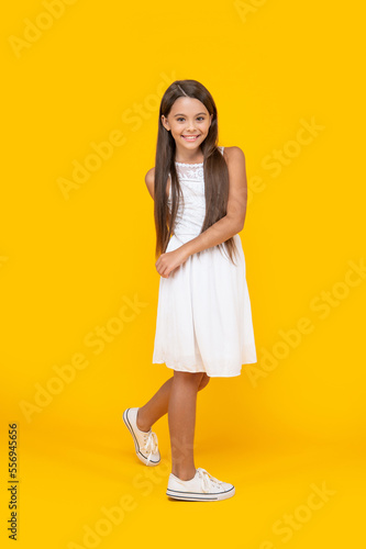 positive teen child in white dress standing on yellow background
