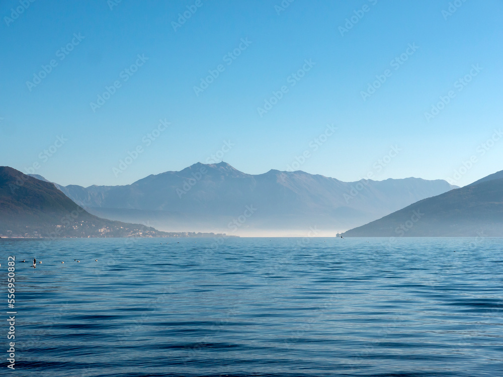 Seascape in heavy mist surrounded by mountains under blue sky view from water surface