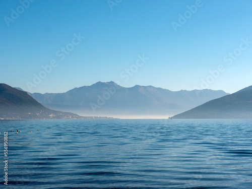 Seascape in heavy mist surrounded by mountains under blue sky view from water surface