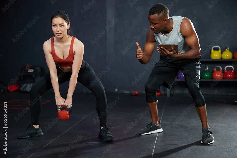 athletic young woman training with kettlebell with coach or personal trainer in the gym athletic young woman training with kettlebell with coach or personal trainer in the gym