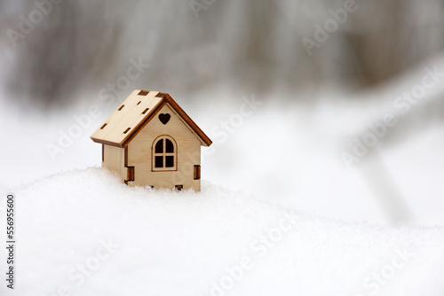 Wooden house model in a snow on winter forest background. Concept of country cottage, real estate in ecologically clean area