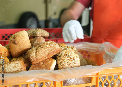 Lebensmittelspende Tafel: Ehrenamtlicher Mann mit Handschuhen und Schürze packt (Bewegungsunschärfe) verschiedene Brötchen und Brot in eine große Kiste für die Verteilung an Bedürftige