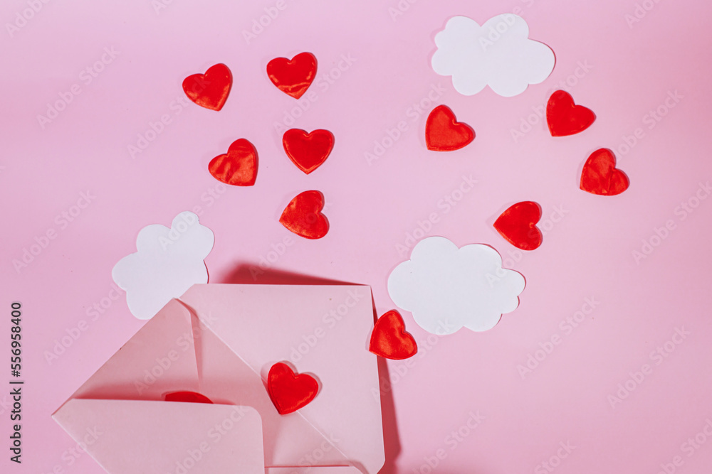 An open postal envelope with red hearts and clouds flying out of it. Hearts flying out of an open craft envelope. Paper clouds on a pink background. Declaration of Love