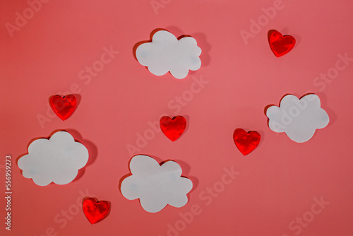 White paper clouds and red textile hearts on a red background. Conceptual background for Valentine's Day or Women's Day. Copy space