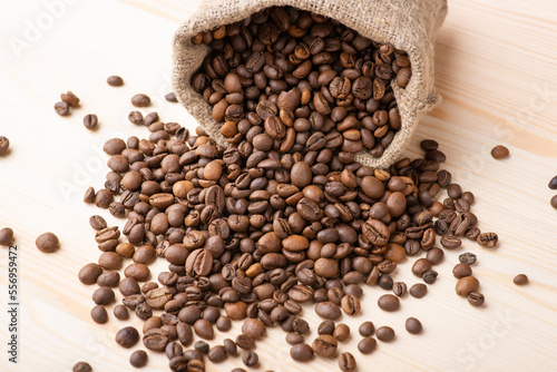 Roasted coffee beans falling from linen bag on wooden table. Beautiful composition of coffee grain