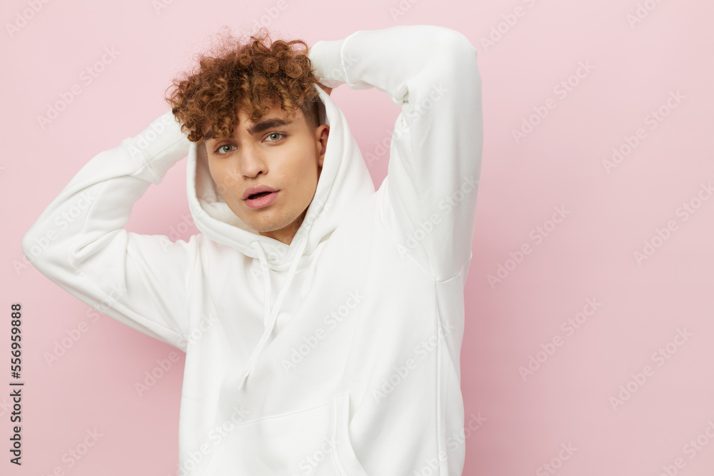 a handsome, attractive man stands on a pink background in a stylish white hoodie with a hood on his head and holds it with his hands behind his head a handsome, attractive man stands on a pink background in a stylish white hoodie with a hood on his head and holds it with his hands behind his head