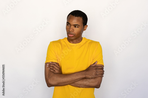 Portrait of confident young man posing with folded arms against white background. African American guy wearing yellow T-shirt looking away with thoughtful expression. Confidence concept