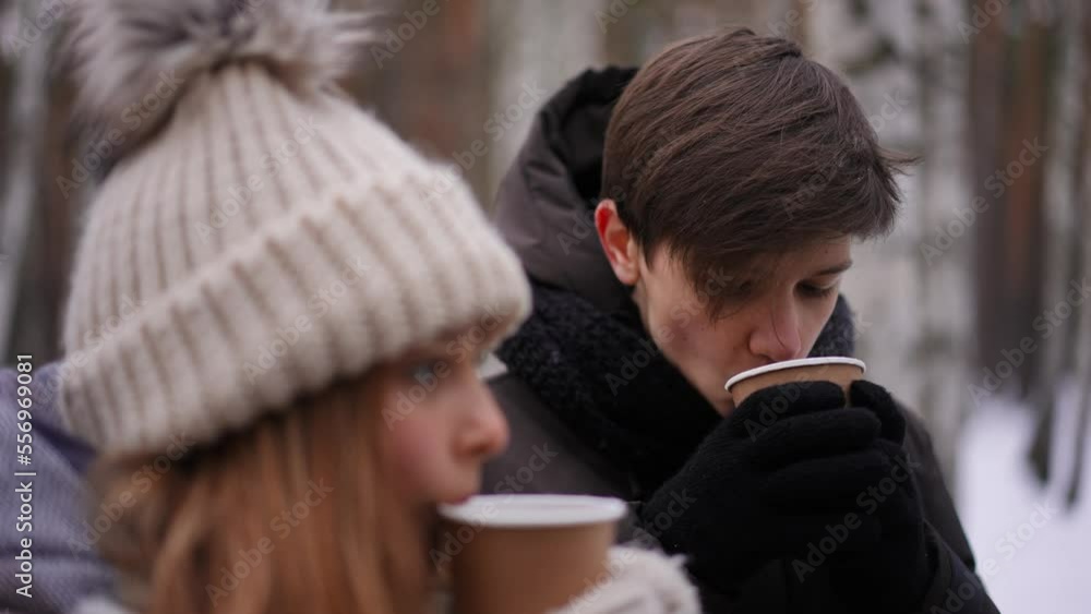 Teenage Caucasian boy drinking hot tea standing with girl in winter park outdoors. Portrait of handsome loving boyfriend dating with girlfriend smiling. Lifestyle and relationship concept Teenage Caucasian boy drinking hot tea standing with girl in winter park outdoors. Portrait of handsome loving boyfriend dating with girlfriend smiling. Lifestyle and relationship concept