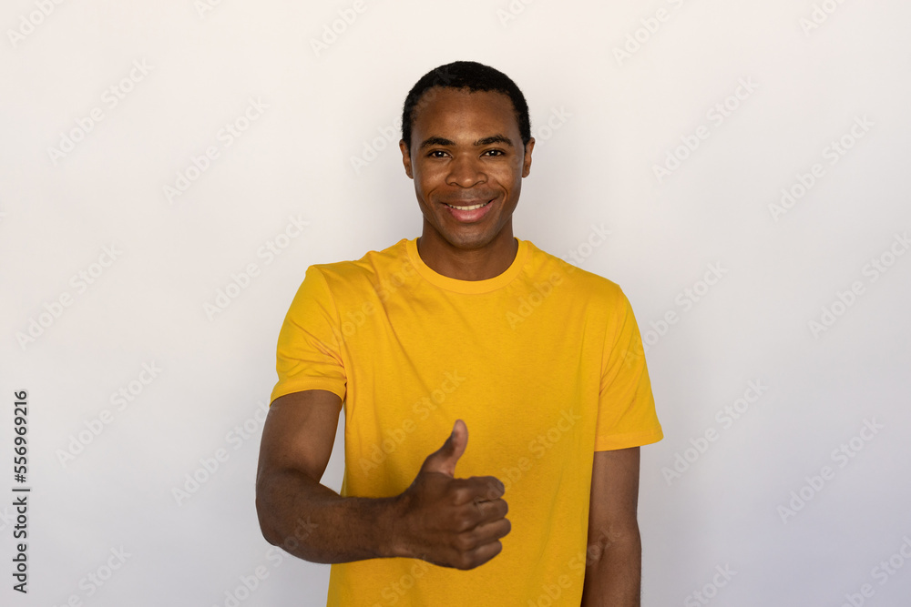 Portrait of happy young man making like gesture against white background. African American guy wearing yellow T-shirt showing thumb up. Approval concept Portrait of happy young man making like gesture against white background. African American guy wearing yellow T-shirt showing thumb up. Approval concept