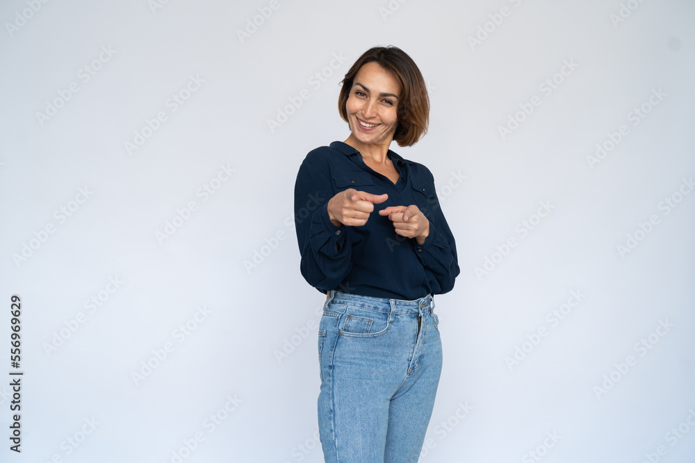 Joyful woman pointing at camera. Female model in dark blue shirt smiling and pointing at camera, choosing someone. Portrait, studio shot, employment concept Joyful woman pointing at camera. Female model in dark blue shirt smiling and pointing at camera, choosing someone. Portrait, studio shot, employment concept