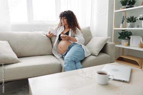 Pregnant woman smile blogger takes vitamins and medicines sitting on the couch at home freelancer in the last month of pregnancy lifestyle before childbirth