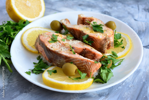 roasted steaks of salmon on white plate decorated with lemon, parsley and green olives