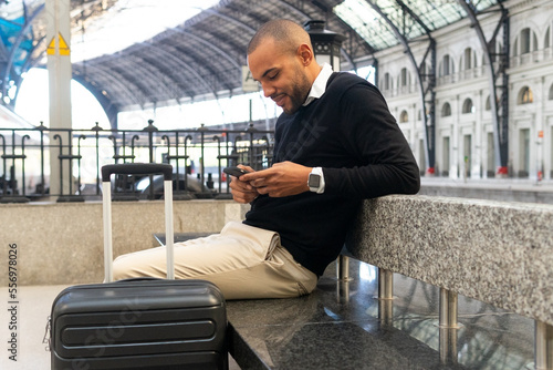 Smiling black businessman chatting on smartphone while sitting at train station photo