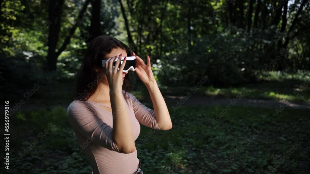 Nature outdoors background, technology and people concept, young woman in VR glasses plays video games outdoors in the park at sunset against a blurred background of nature Nature outdoors background, technology and people concept, young woman in VR glasses plays video games outdoors in the park at sunset against a blurred background of nature