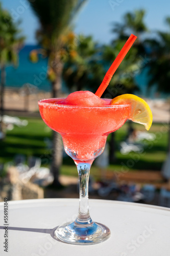 Colourful cold Strawberry daiquiri cocktail drink served in glass at outdoor cafe overlooking blue sea and palm trees, relax and holidays at sea