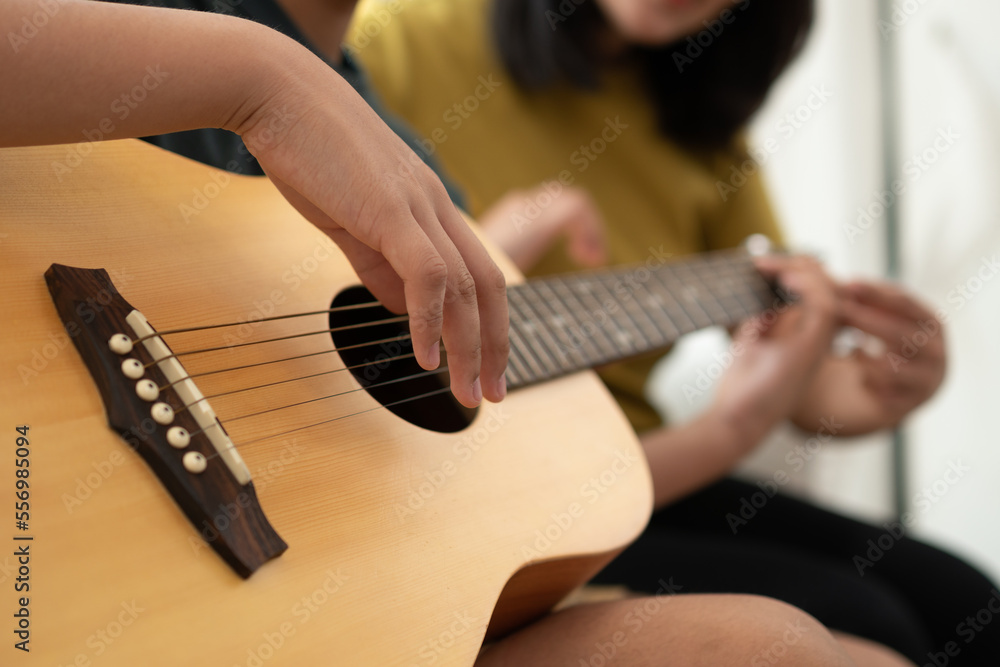 Naklejka premium Asian boy playing guitar with mom in the living room for teaching him son play guitar, feel appreciated and encouraged. Concept of a happy family, learning and fun lifestyle, love family ties