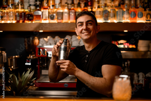 Authentic smiling male barman in bar interior with shaker making alcohol beverages