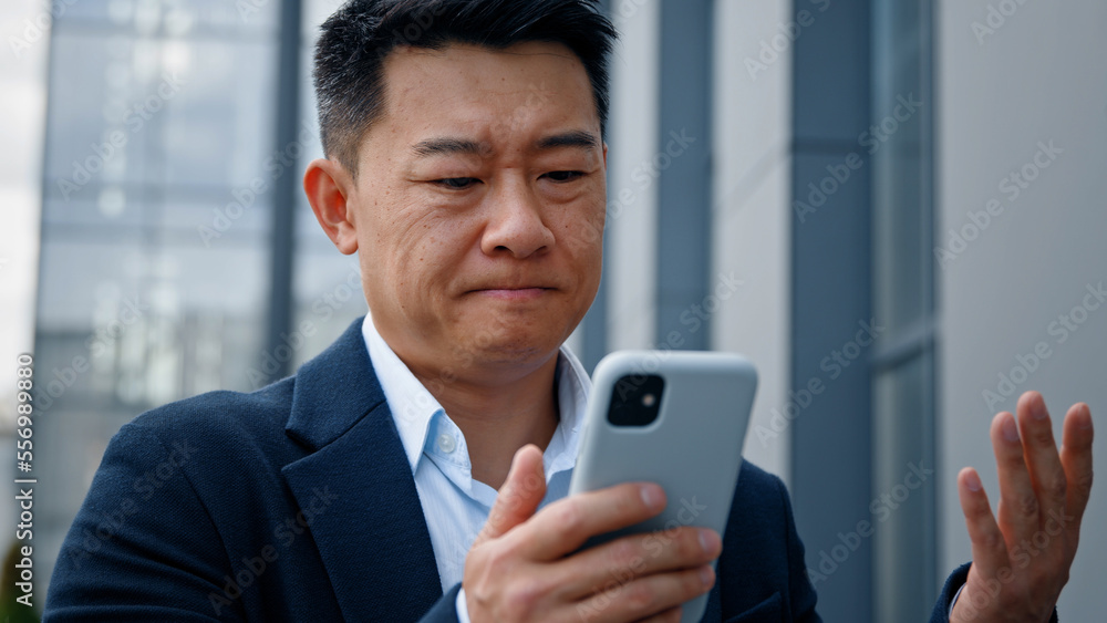 Sad Asian middle-aged adult man mad unhappy businessman feeling annoyed with using broken smart phone low battery problem angry having problem with mobile telephone frustrated bad news outdoors Sad Asian middle-aged adult man mad unhappy businessman feeling annoyed with using broken smart phone low battery problem angry having problem with mobile telephone frustrated bad news outdoors