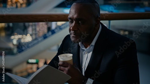 Ethnic male African man businessman employer entrepreneur drinking tea aromatic hot coffee at table in cafe cafeteria restaurant drink latte cappuccino enjoying reading book read notebook text study