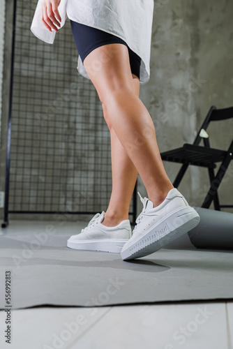 Beautiful woman in youth leather white sneakers and standing on white background. Women's legs with fashionable shoes. Casual white women's shoes