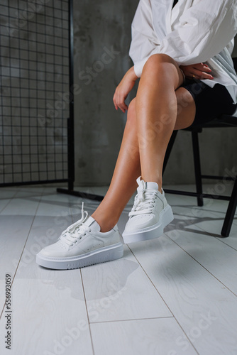 Beautiful female legs in leather white casual sneakers. Women's legs with fashionable shoes. Casual white women's shoes
