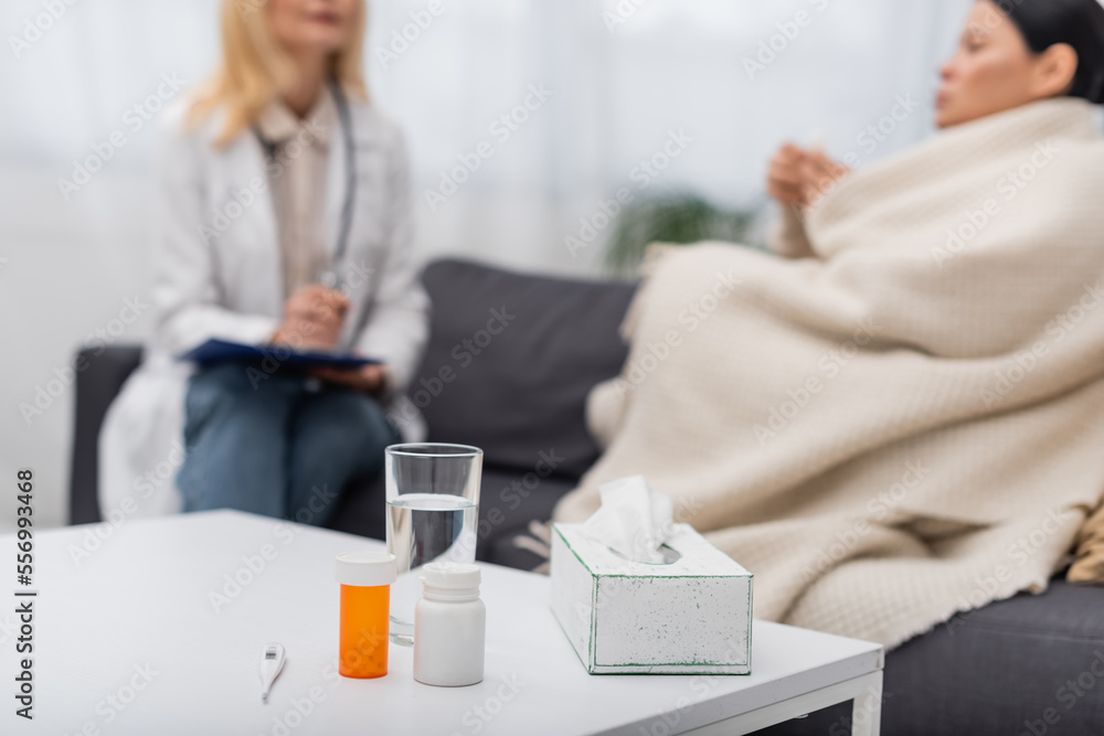 Obraz premium Pills and glass of water near blurred woman and doctor at home