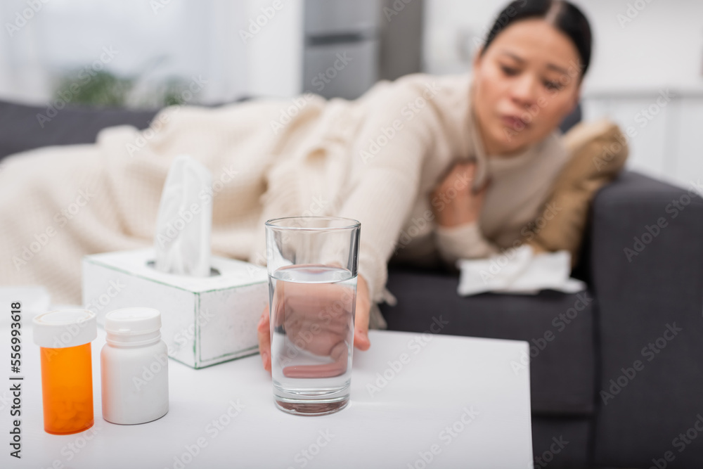 Blurred woman taking glass of water near pills and napkins at home Blurred woman taking glass of water near pills and napkins at home