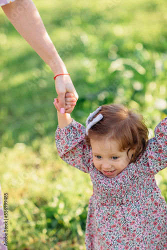 a cute little girl holds the hands of mom and dad on a walk in the park. 