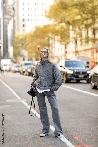 full length of stylish woman in sunglasses and grey outfit holding black handbag and standing on street of New York city