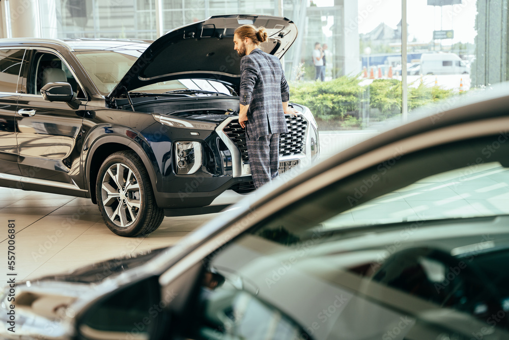 Obraz premium Young man looking at the new car. Consumer in car dealership.