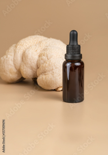Bottle of dark amber glass with essential oil against beautiful lion mane mushroom on beige background