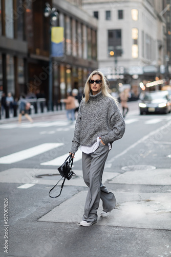 full length of blonde woman in knitted sweater and sunglasses walking with hand in pocket on urban street in New York © LIGHTFIELD STUDIOS