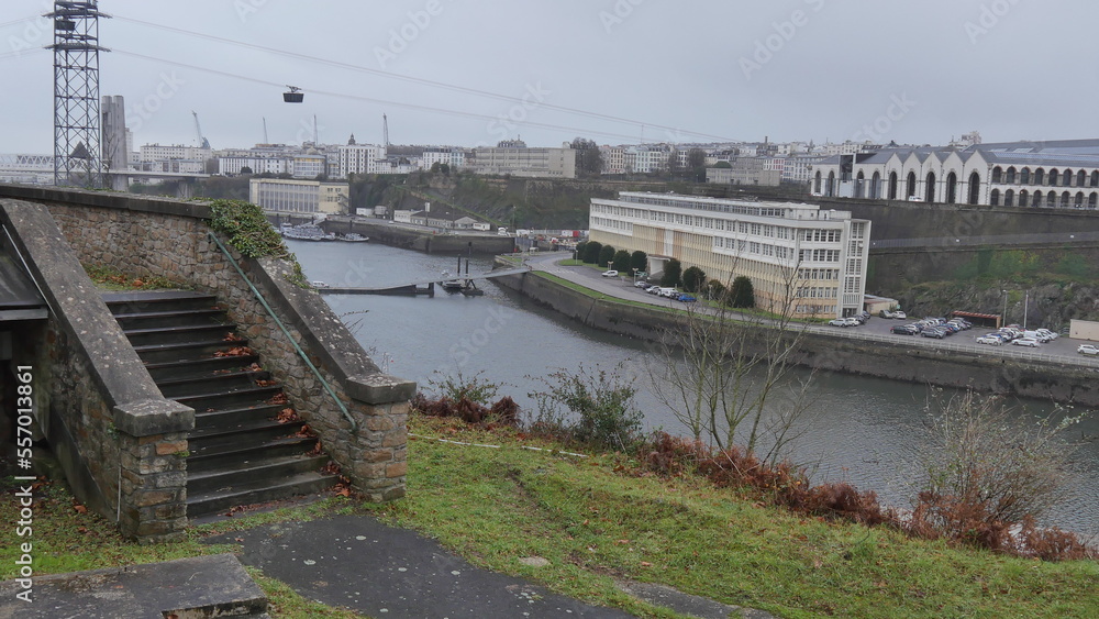 L'arsenal de Brest et tout l'équipement militaire et maritime, base militaire en plein milieu de la ville, sous un ciel nuageux et gris, pluvieux, des bateaux accostés dans l'eau ou dans le fleuve