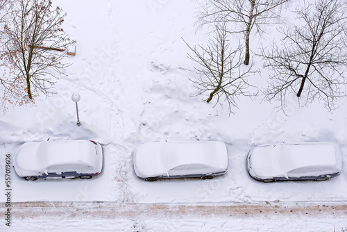 Cars covered in snow parked in row on parking lot in winter seson, top view. Parked cars covered with snow after snow storm.