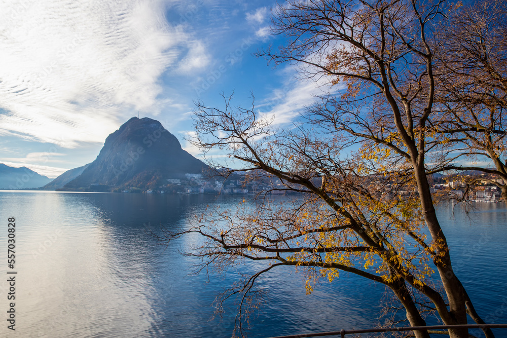 Amazing view on park with autumn leaf color and Lugano town on other side of lake and San Salvatore mount