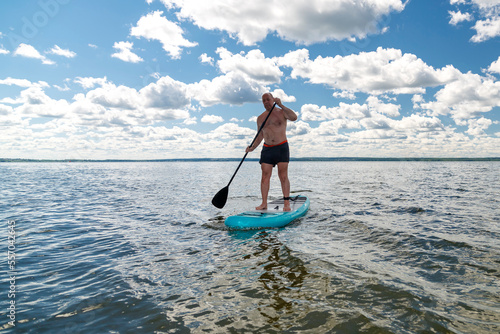 A man on a SUP board with a paddle in the lake against the background of white clouds.