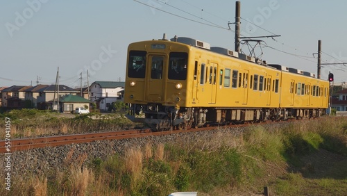 夕暮れ時の田舎を走る黄色いワンマン電車