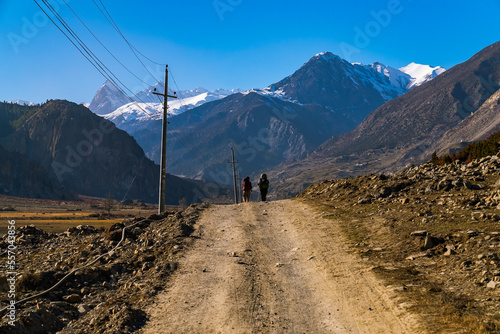 Two trekkers walking down a dirt road with himalyan mountains in the distance on the Annapurna Circuit Trek photo