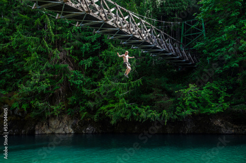 Athletic adventurous male jumping off a high bridge into a river. photo