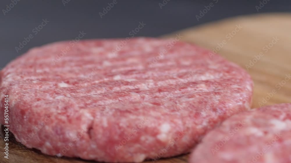 Camera movement from top to bottom along three raw burger patties lying on a wooden board on a dark background of a table surface. Making hamburgers. Camera movement from top to bottom along three raw burger patties lying on a wooden board on a dark background of a table surface. Making hamburgers.