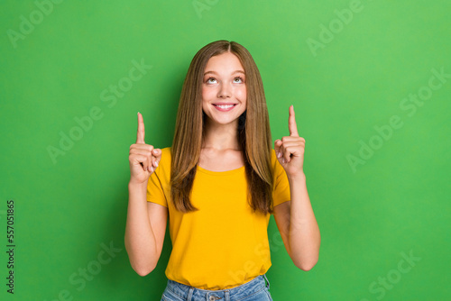 Photo of cheerful adorable girl toothy smile look direct fingers up empty space isolated on green color background