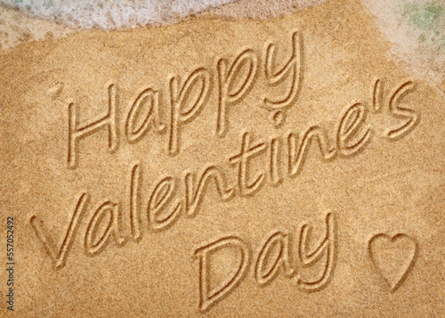 Happy Valentine's Day message handwritten on smooth sand beach with incoming wave
