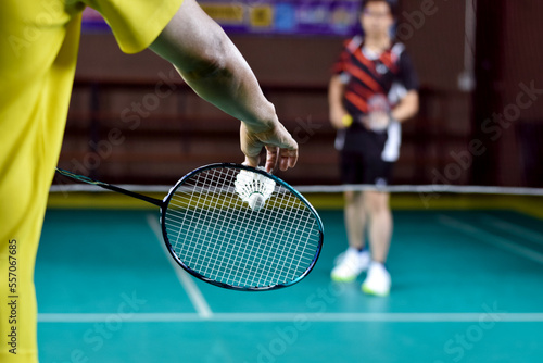 Badminton racket and old white shuttlecock holding in hands of player while serving it over the net ahead, blur badminton court background and selective focus.