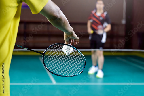 Badminton racket and old white shuttlecock holding in hands of player while serving it over the net ahead, blur badminton court background and selective focus.