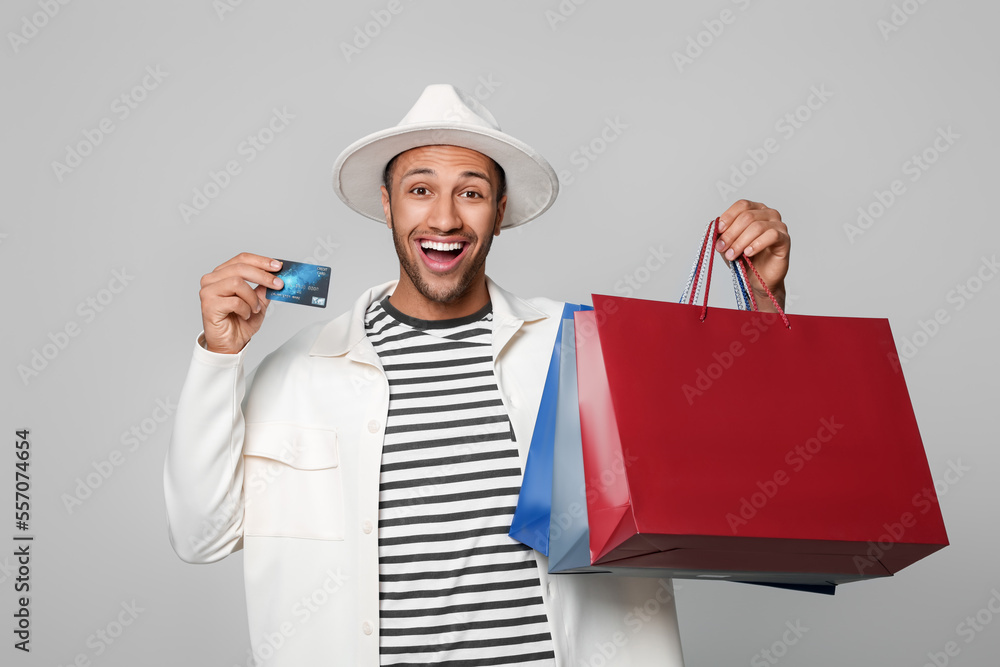 Happy African American man in hat with shopping bags and credit card on light grey background Happy African American man in hat with shopping bags and credit card on light grey background