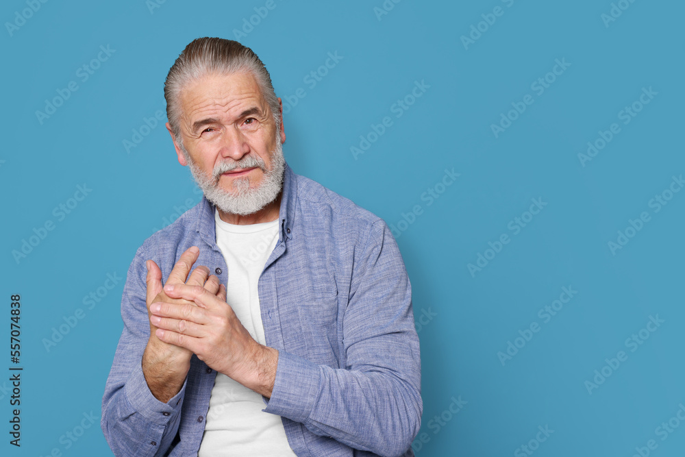 Senior man suffering from pain in hand on light blue. Arthritis symptoms Senior man suffering from pain in hand on light blue. Arthritis symptoms