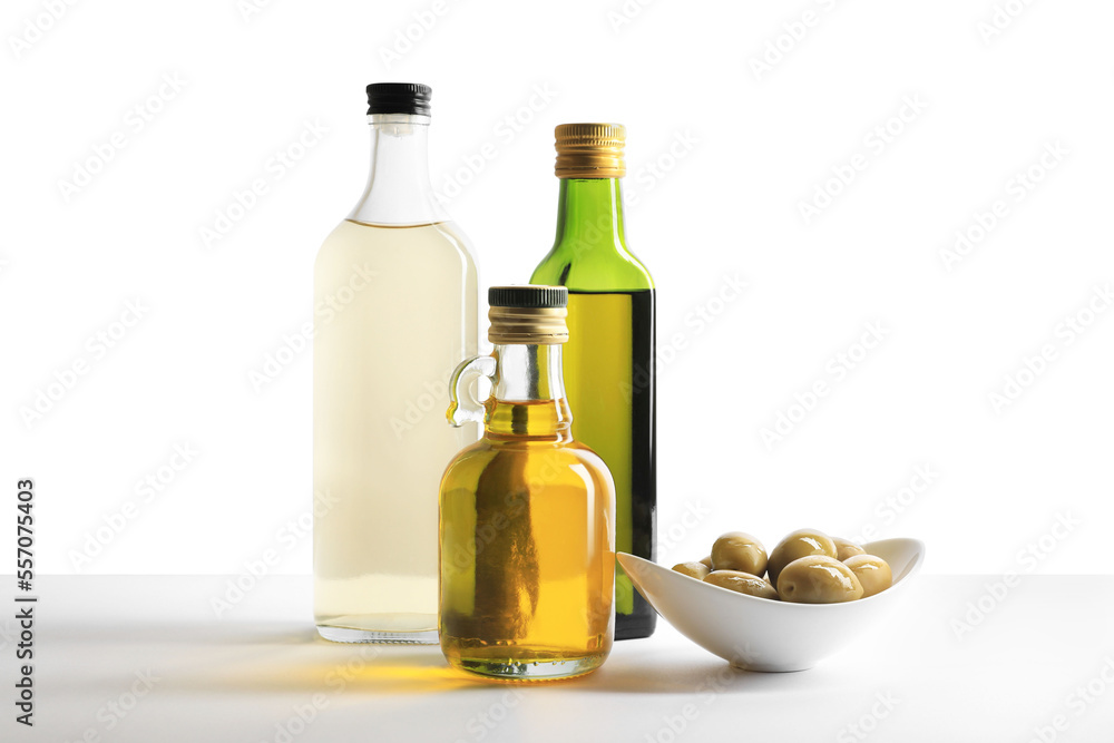 Bottles of different cooking oils and olives on white background