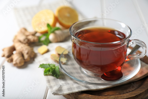 Cup of delicious ginger tea and ingredients on white wooden table, closeup. Space for text